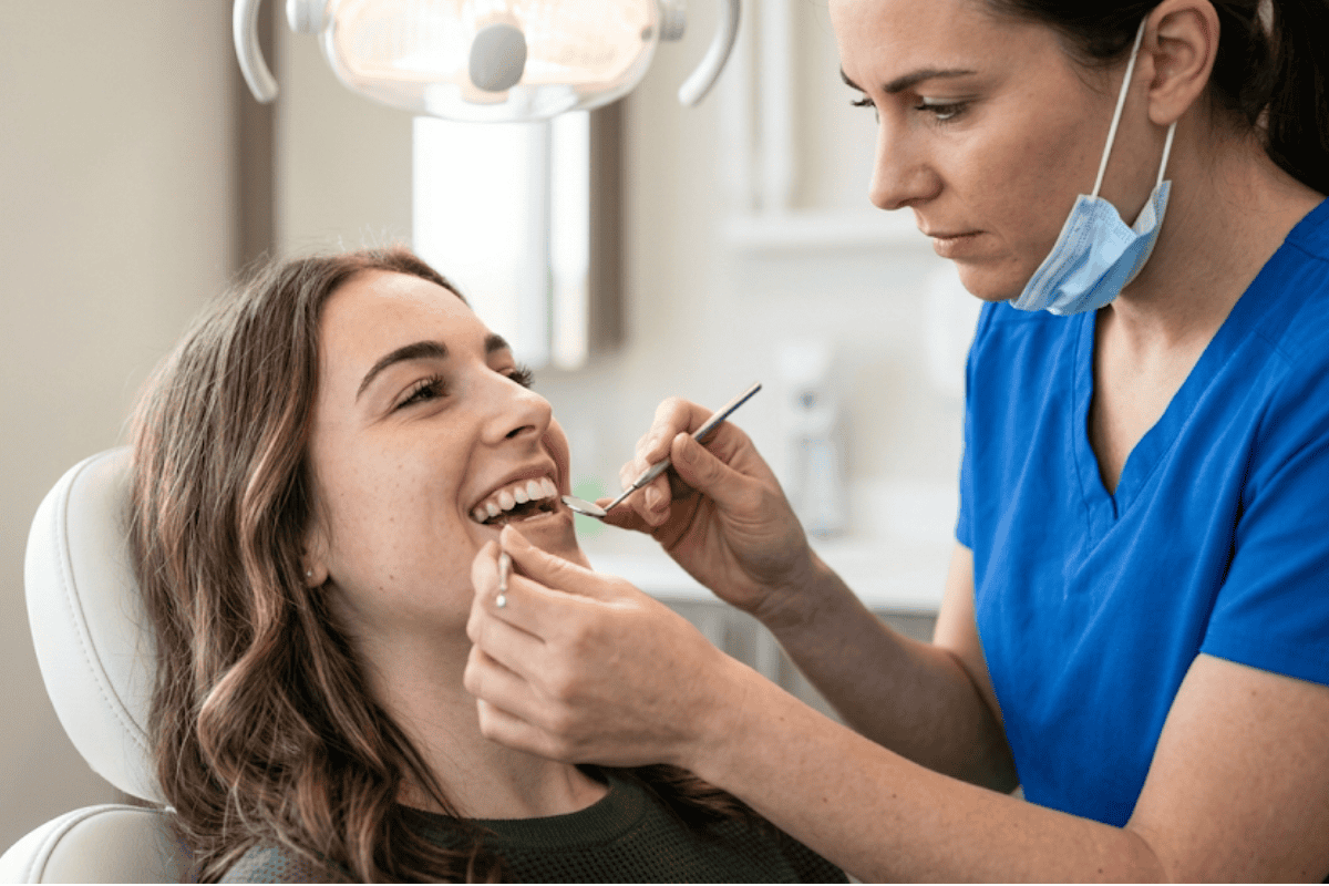 Dental hygienist in blue scrubs works on a patient’s teeth with dental tools at a clinic chair.